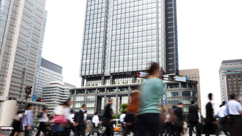 People blurred out walking behind tall corporate office tower