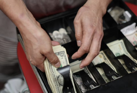 Hands pulling American bills out of a cash register
