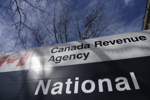 A Canadian Revenue Agency sign in front of bare tree branches and blue sky