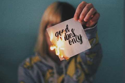 Photo of a person burning a paper that says "good vibes only" in cursive writing