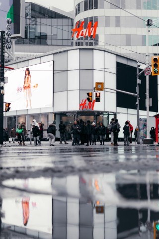 A low-to-the-ground shot of H and M at Yonge and Dundas in Toronto with a reflection of the storefront in a puddle.