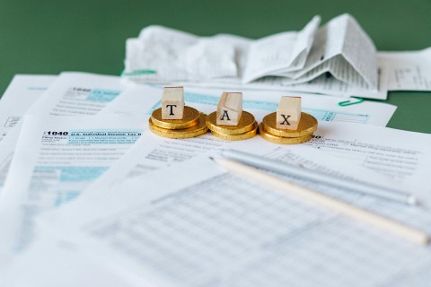 letters T A X on stacks of coins on top of tax papers